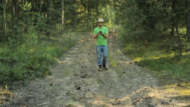 Un hombre camina por el bosque con el teléfono y mira la aplicación de navegación. Él elige la dirección correcta — Vídeo de stock