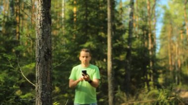 Bir adam telefonla ormanda yürür ve navigasyon uygulamasıbakar. Doğru yönü seçiyor.