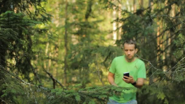 Un homme marche dans la forêt avec le téléphone et regarde l'application de navigation. Il choisit la bonne direction — Video