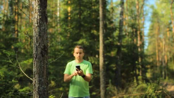 Um homem caminha pela floresta com o telefone e olha para o aplicativo de navegação. Ele escolhe a direcção certa. — Vídeo de Stock