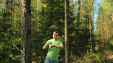 Bir adam akıllı saat ile ormanda yürür ve navigasyon uygulaması bakıyor. Doğru yönü seçiyor.