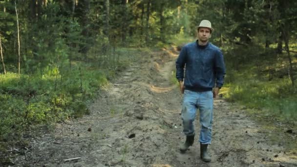 Ung vandrare man med hatt promenader i skogen. Han justerar sina gamla jeans och fortsätter — Stockvideo