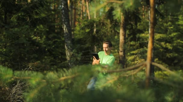 Um homem caminha pela floresta com um tablet PC e olhando para o aplicativo de navegação. Ele escolhe a direcção certa. — Vídeo de Stock