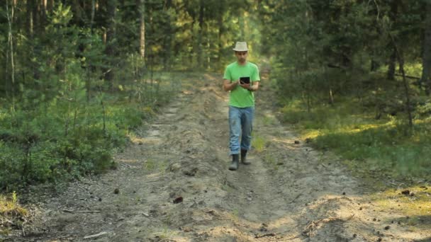 Un uomo cammina attraverso la foresta con un tablet PC e guardando l'applicazione di navigazione. Egli sceglie la direzione giusta — Video Stock