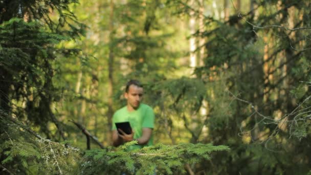Un homme marche dans la forêt avec une tablette PC et regarde l'application de navigation. Il choisit la bonne direction 