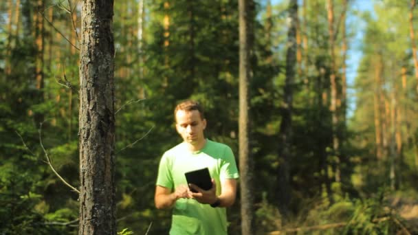 ある男性がタブレットPCを持って森の中を歩き、ナビゲーションアプリケーションを見ます。彼は正しい方向を選ぶ — ストック動画