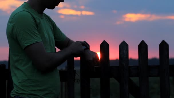 男は日没時にスマートウォッチを見て触れます。美しい赤い空と森の後ろの太陽 — ストック動画