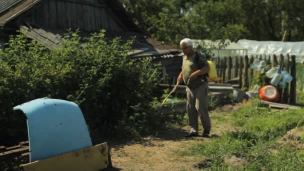 Человек работает с садовым спреем в поле рядом с домом — стоковое видео