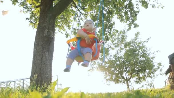 Söt baby boy spelar på swing i sommarträdgården. Gungor är kopplade till trädet — Stockvideo