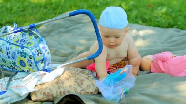 Charmiga pojke leker i trädgården med en liten docka och barnvagn — Stockvideo