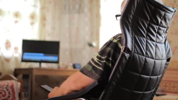 वरिष्ठ माणूस लेदर खुर्चीवर बसला आणि घरी चॅनेल टीव्ही रिमोट कंट्रोल बदलतो — स्टॉक व्हिडिओ