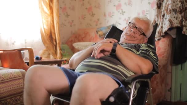 Homme âgé est assis avec horloge intelligente dans une chaise en cuir près de la maison TV. Un homme regarde le message par une montre intelligente — Video