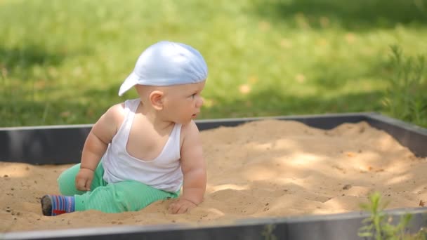 Lindo niño jugando con arena en una caja de arena. Parque de verano y césped verde en el fondo — Vídeos de Stock