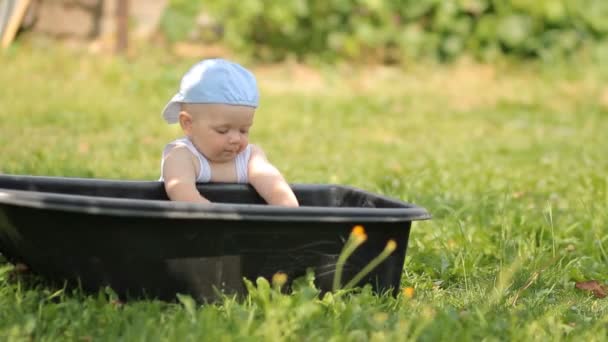 Adorable niño jugando con una cuenca de agua en el jardín. Se levanta y sonríe — Vídeos de Stock