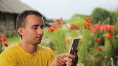 Genç adam telefonda bahçede çiçek yakınındaki arıyor. Beyaz, kırmızı ve mor çiçekler içinde belgili tanımlık geçmiş