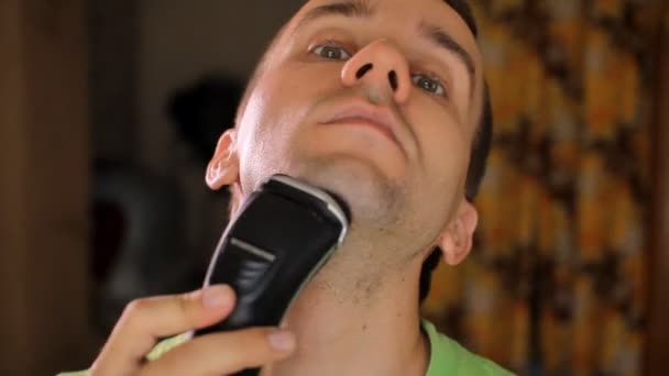 Handsome young man shaving with electric razor. Electric shaver in living room — Stock Video