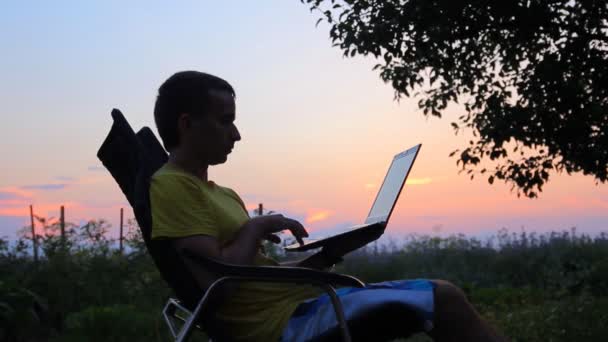 Slhouette van happy zakenman met laptop en thee op het veld bij zonsondergang — Stockvideo