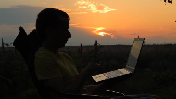 Slhouette of happy business man with laptop working on the field at sunset time — Stock Video