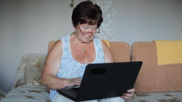 Nő ül a kanapén, otthon szemüveg koncentrálva, mint ő szerkezet-ra egy laptop — Stock videók