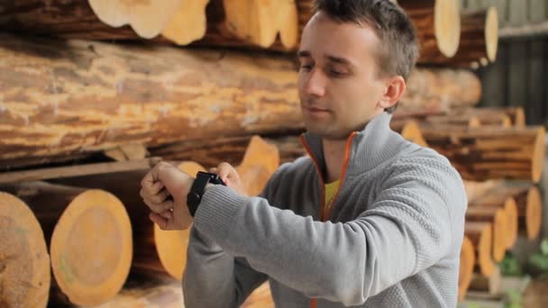 Joven ingeniero forestal toque reloj inteligente en frente de la madera — Vídeo de stock