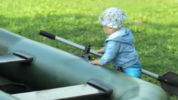 Schöner kleiner Junge, der mit einem Schlauchboot und einem Paddel spielt. Das Boot liegt auf dem Gras im Garten. Fischerei in der Zukunft — Stockvideo