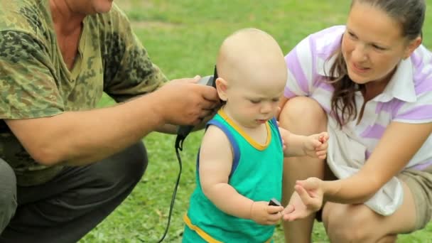 Mutter und Großvater schneiden Babyhaare mit Haarschneidemaschine im heimischen Garten — Stockvideo