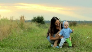 Alanını oynayan bebek ile mutlu bir aile. Gün batımından önce güzel turuncu gökyüzü. Gülümsüyor ve sevinç