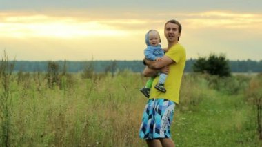 Alanını oynayan bebek ile mutlu bir aile. Gün batımından önce güzel turuncu gökyüzü. Gülümsüyor ve sevinç