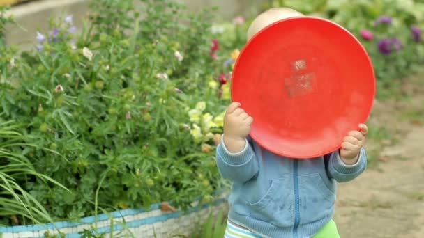 Szép baby boy játék-val egy lemezt a frizbi. Ő megnyitja és bezárja az arc és a kamera mosolyogva. boldog gyermekkor fogalma — Stock videók