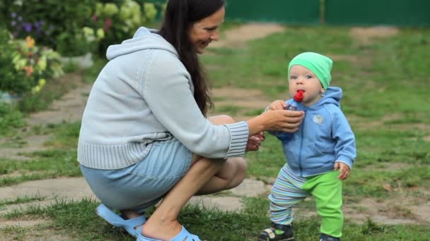 Hijo sosteniendo una botella de agua y madre sosteniéndolo en sus brazos. tiro al aire libre en el jardín . — Vídeos de Stock