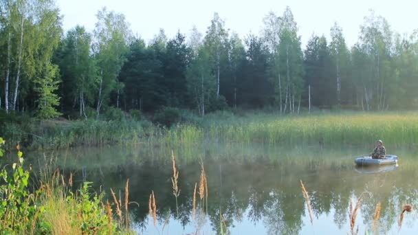 Рибалка плаває на озері на надувному човні з вудкою. Рано вранці з туманом на воді. відпустка в дикій природі — стокове відео