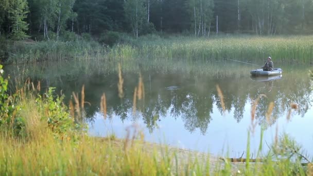 Il pescatore galleggia su un lago su una barca gonfiabile con una canna da pesca. Mattina presto con nebbia sull'acqua. vacanza in natura — Video Stock