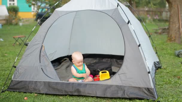 Schönes Baby spielt mit einem großen Zelt auf dem Rasen. Baby unter einem Jahr, in grünem T-Shirt und Spielzeug im Zelt. — Stockvideo