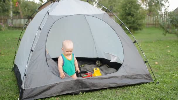 Bebê bonito está brincando com uma grande tenda na grama. Bebê menos de um ano, em uma camiseta verde e brinquedos dentro da tenda . — Vídeo de Stock