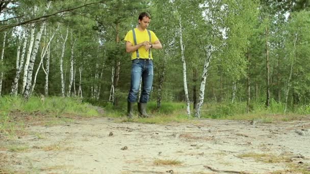 Homem caminhante caminhando pela floresta e toque relógio inteligente. T-shirt amarela e jeans com suspensórios. Tecnologia na natureza — Vídeo de Stock