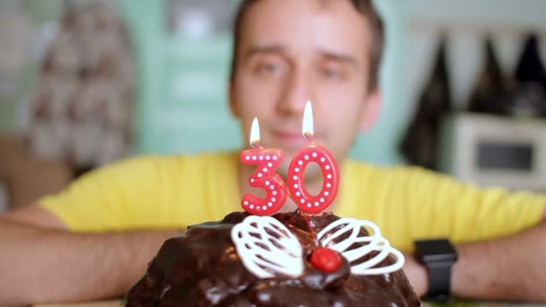 El hombre sopla las velas 30 años en un pastel de chocolate con alas de mariposa. El hombre cumple años hoy. . — Vídeos de Stock