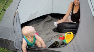 Anne ve güzel yürümeye başlayan igratyut çimenlerin üzerinde büyük bir palatkye. Bebek yeşil tişört ve oyuncak çadır içinde bir yıldan az.