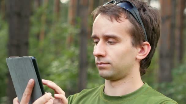 Pohledný muž středního věku v gren tričko sezení touch tablet. Usmívá se, letní les na pozadí. Detail — Stock video