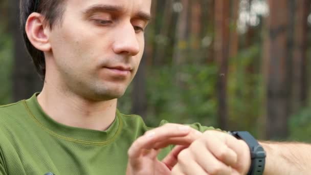 Il giovane tocca l'indossabile in un parco. T-shirt verde. Leggi il messaggio e sorridi. Primo piano — Video Stock