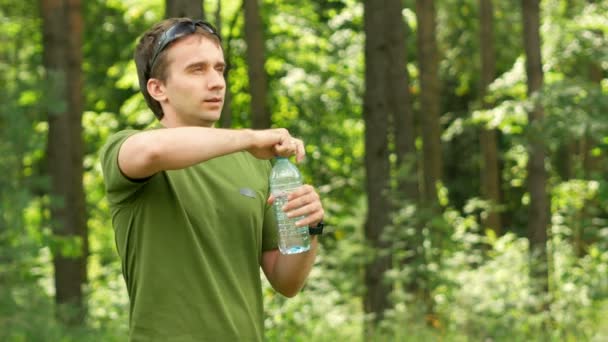 Fiatal férfi kerékpáros iszik víz egy üveg a parkban. Zöld póló és napszemüveg — Stock videók