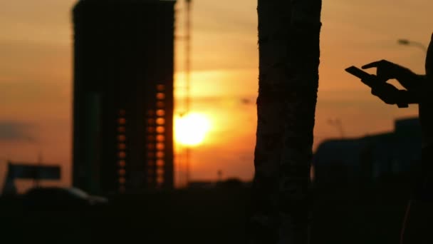 平板电脑和手在日落时的剪影。太阳冲破建造的摩天大楼 — 图库视频影像