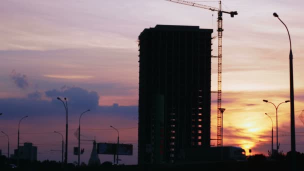 Proyecto de construcción silueta contra la puesta del sol cielo. Paisaje urbano con coches y obra — Vídeos de Stock