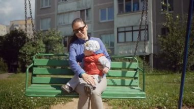 Mutlu genç kadın ve bir oyun alanı üzerinde sallanan bir küçük oğlu