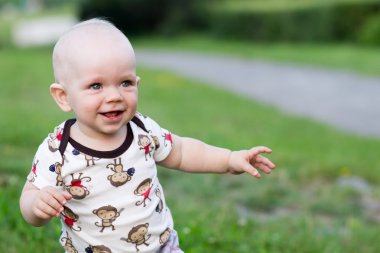 Sevimli bebek çocuk oynarken ve parkta gülüyor. Yaz kırıntıları için yeşillik ilginç şeyler bir sürü civarındadır. Çocuk 1 yıl