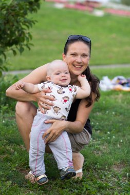 Parkta anne ile First Steps erkek bebek. Yazın bir sürü yeşil çimen ve ağaç etrafında.