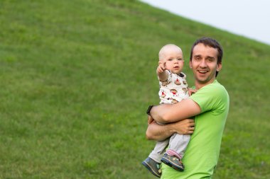 Parkta babası ile First Steps erkek bebek. Yazın bir sürü yeşil çimen ve ağaç etrafında.