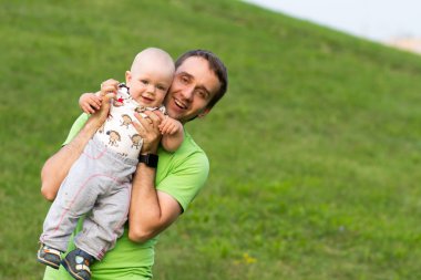 Parkta babası ile First Steps erkek bebek. Yazın bir sürü yeşil çimen ve ağaç etrafında.
