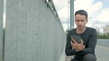 Dijital tablet ile modern genç adam açık portresi. Yolun ve güzel mavi bulutlar içinde belgili tanımlık geçmiş köprünün korkuluk