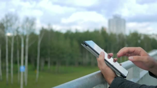 Retrato al aire libre de un joven moderno con tableta digital.Sobre el fondo de árboles verdes y hermosas nubes azules. Primer plano — Vídeo de stock