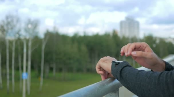 Ritratto all'aperto di giovane uomo moderno con orologio intelligente. Sullo sfondo di alberi verdi e bellissime nuvole blu. Primo piano — Video Stock
